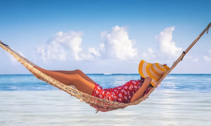 femme avec un chapeau allongée dans un hamac face à une mer turquoise en république dominicaine