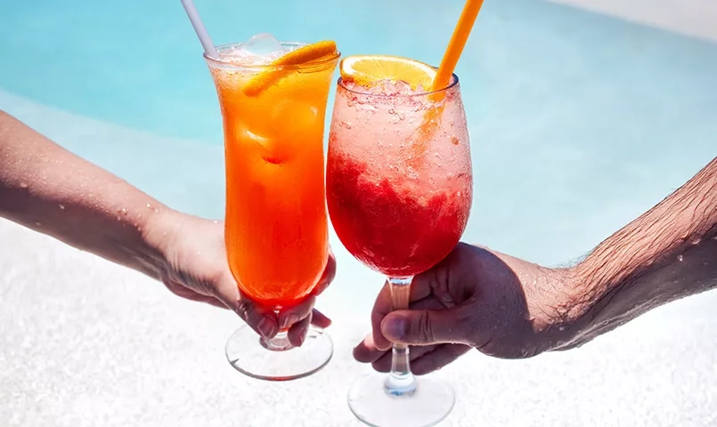 2 personnes tenant un cocktail au bord d'une piscine