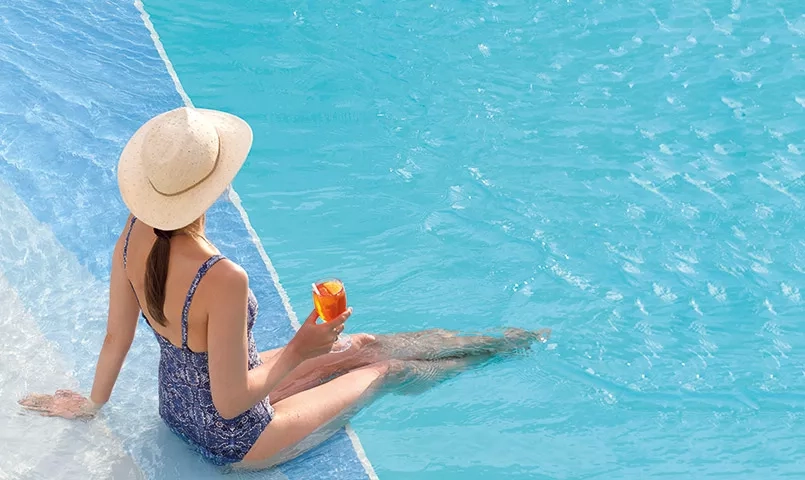 Femme avec un cocktail dans les main et les pieds dans l'eau d'une piscine