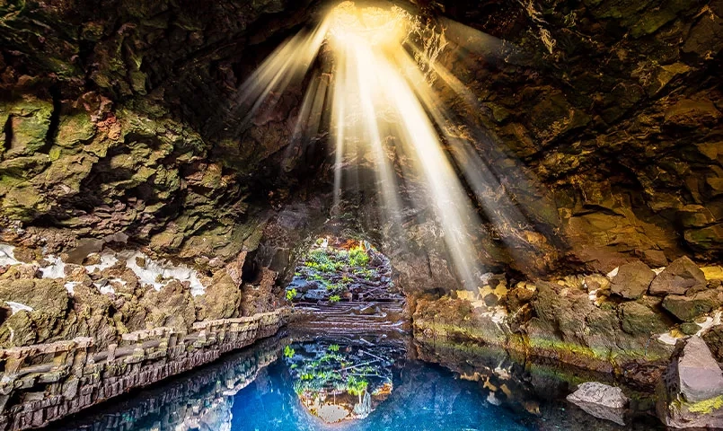Grotte avec des rayons de soleil illuminant un bassin d'eau bleue. 