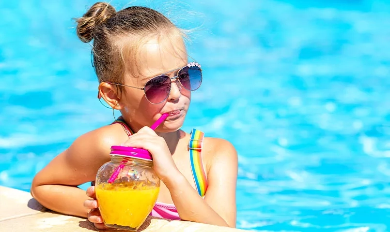 Une fille avec des lunettes de soleil boit une boisson au bord d'une piscine.
