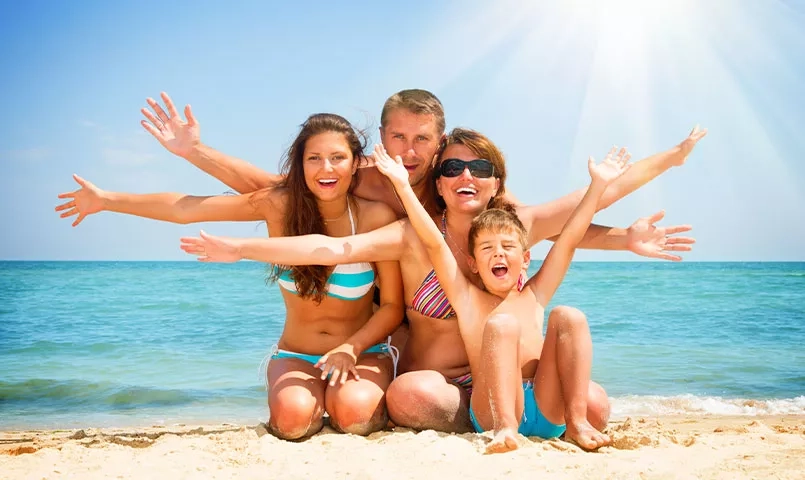 Une famille pose joyeusement sur une plage, avec la mer en arrière plan.