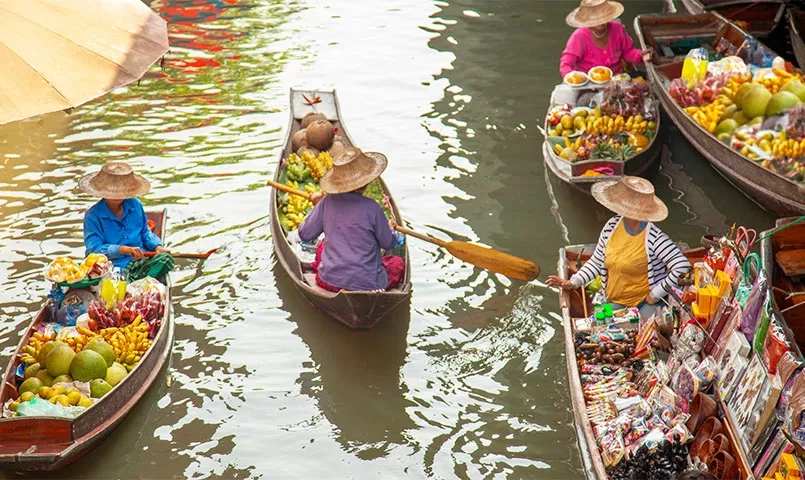 Des marchands dans des bateaux chargés de fruits et légumes colorés naviguent sur un canal. 