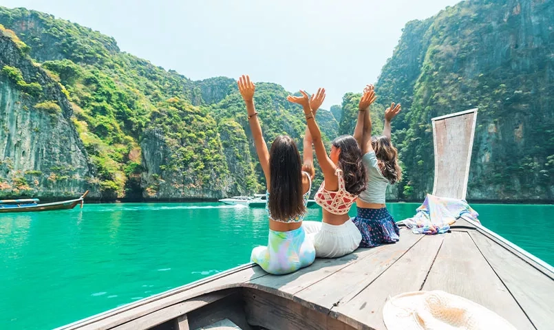 Trois amies sur un bateau admirent le paysage de falaises karstiques et d'eaux turquoise. 