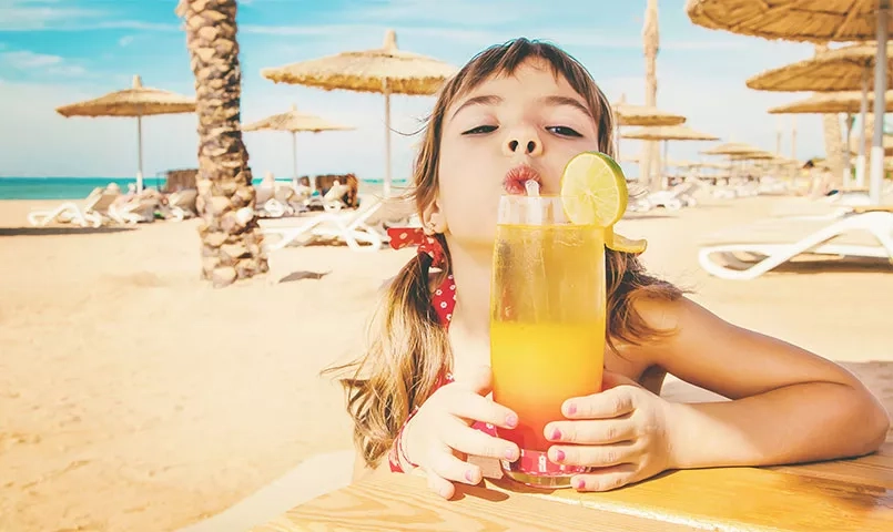 Une fille boit un cocktail sur une plage ensoleillée.