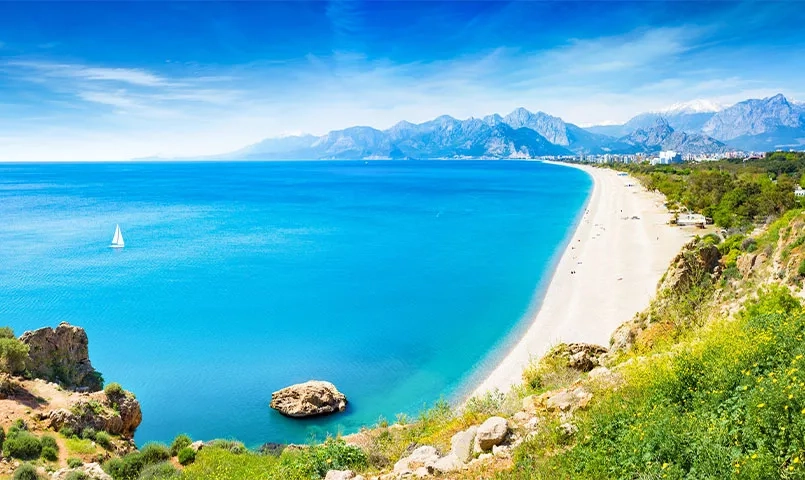Plage de sable blanc bordée par une mer turquoise. 