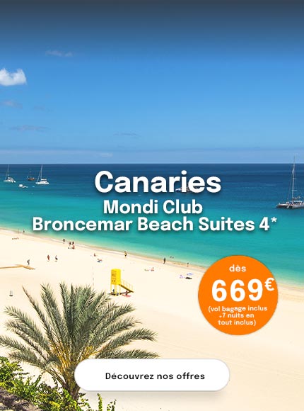 une plage de sable blanc, avec en fond un village de maisons blanches, une mer turquoise avec quelques bateaux